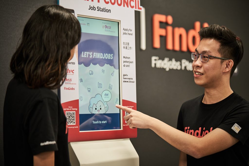 A man pointing at a job kiosk, while a woman looks at the screen of the kiosk