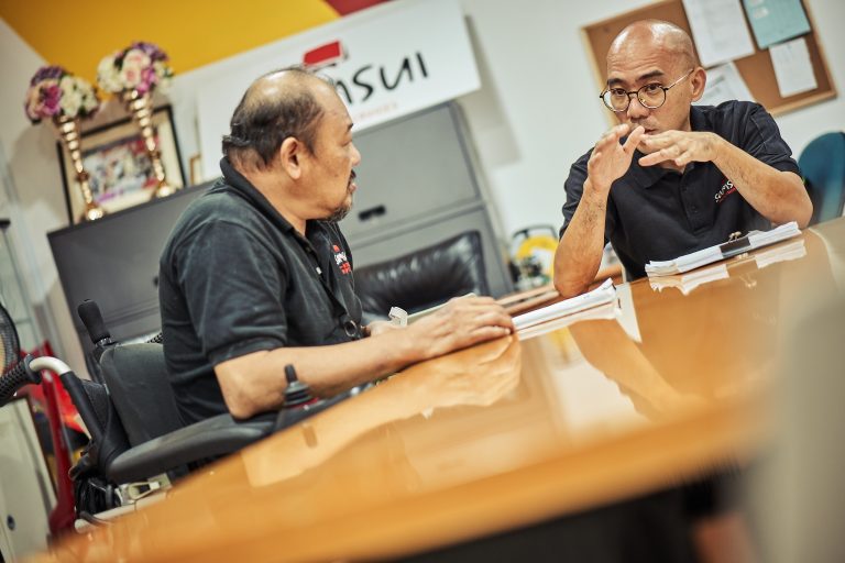 2 men are having a meeting at a table. The man on the left is in a wheelchair