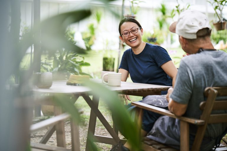 A women seated and smiling while in conversation with a man in a garden